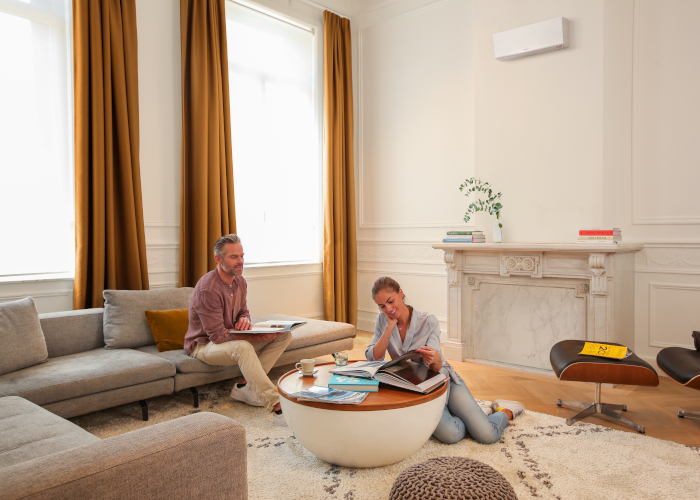 Abkühlung - Frau und Mann sitzen in Wohnzimmer und lächeln - im Hintergrund sieht man eine Klimaanlage der Marke Daikin