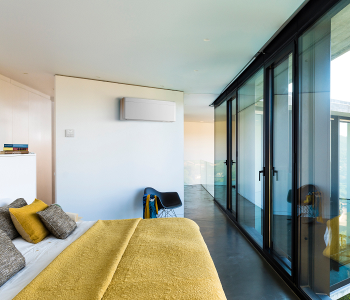 Daikin Klimaanlagen - Wandgerät in Schlafzimmer ober gemütlichem Bett gegenüber von großen Glastüren