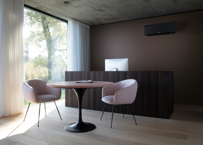 Schwarzes Klimaanlagen Wandgerät an brauner Wand montiert - Tisch mit rosa Sesseln vor Fenster